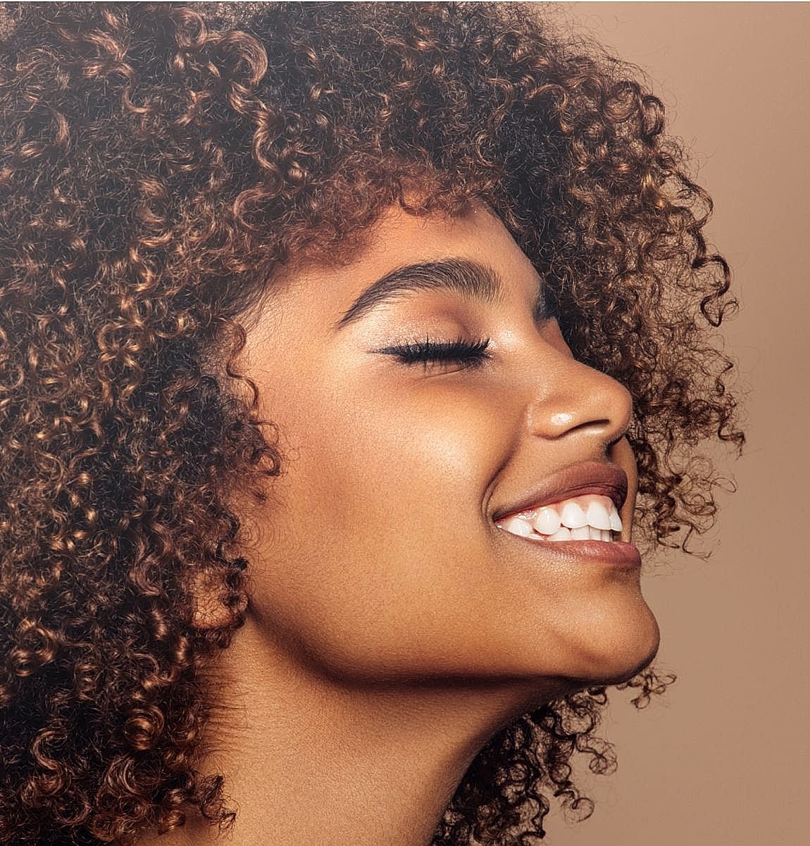 Person with curly hair smiling joyfully.