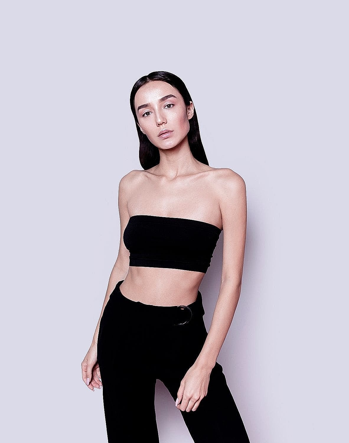 Model wearing black outfit against pastel background.