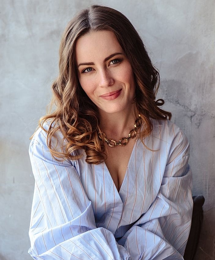 Woman with curly hair smiling in light blue blouse.